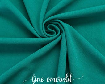 Puede incluir: Primer plano de una tela lisa de color turquesa con una textura fina esmeralda. La tela está doblada y drapeada, mostrando su naturaleza suave y fluida.