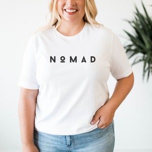 May include: White t-shirt with the word "NOMAD" printed in black letters.