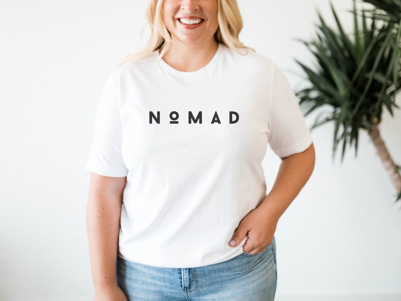 May include: White t-shirt with the word "NOMAD" printed in black letters.