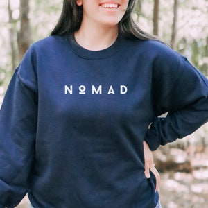 Puede incluir: Una sudadera azul marino con la palabra "NOMAD" impresa en blanco en la parte delantera.