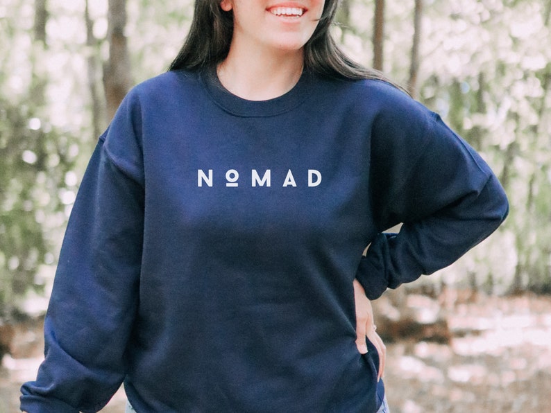 Puede incluir: Una sudadera azul marino con la palabra "NOMAD" impresa en blanco en la parte delantera.