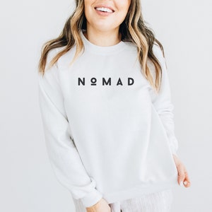 Puede incluir: Sudadera blanca con la palabra "NOMAD" impresa en negro en la parte delantera.