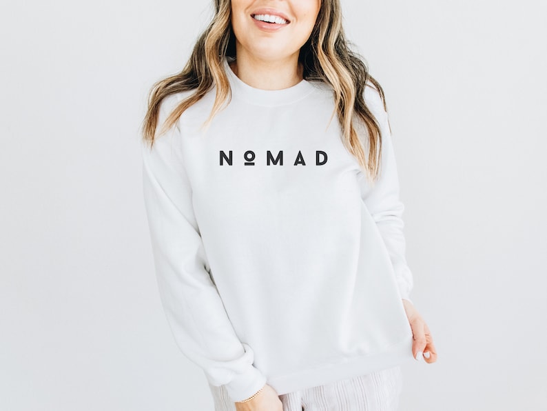 Puede incluir: Sudadera blanca con la palabra "NOMAD" impresa en negro en la parte delantera.