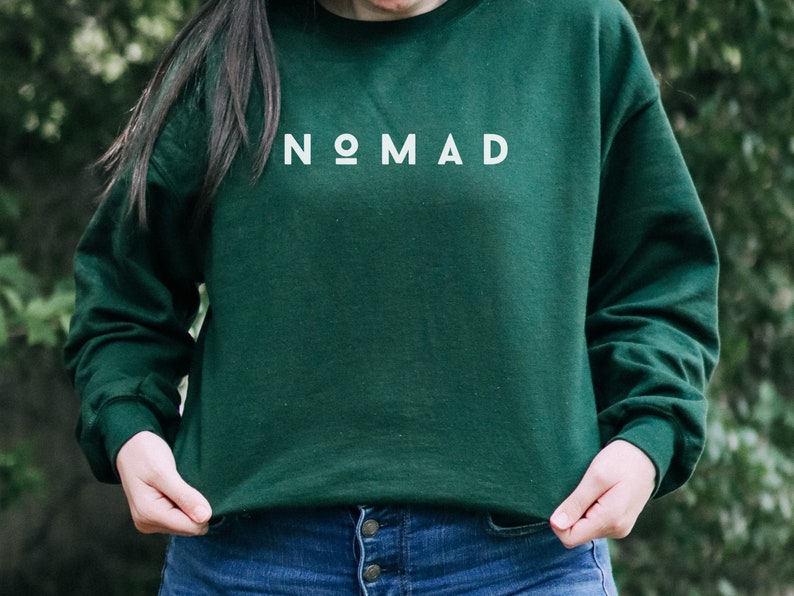 Puede incluir: Una sudadera verde oscuro con la palabra "NOMAD" impresa en blanco en la parte delantera.