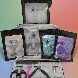 Könnte beinhalten: Ein graues Reiseetui mit verschiedenen Haarstyling-Werkzeugen und Zubehör. Enthält Scheren, Zangen, Kämme, Haargel, Sprühflaschen, Gummibänder, Clips und blaue und lila Haarverlängerungen. Das Etui ist geöffnet und zeigt den Inhalt.
