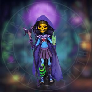 May include: A doll with a yellow skull face, red eyes, and a purple hooded cape. The doll wears a blue textured bodice, a dark purple skirt, and armor. It holds a staff topped with a ram skull and a translucent green object, with a green snake wrapped around one leg.