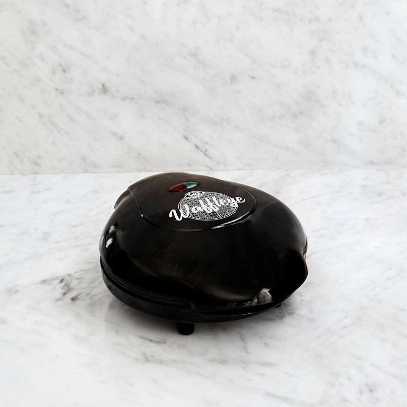 May include: A black waffle maker with a white "Waffleye" logo on the top. The waffle maker has a red and green light indicator.