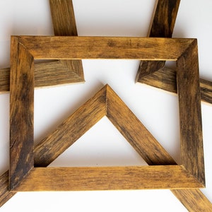 Puede incluir: Cinco marcos de fotos de madera dispuestos en forma de estrella sobre un fondo blanco. Los marcos son todos del mismo tamaño y tienen un acabado marrón oscuro.