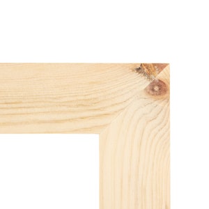 Op de afbeelding: Close-up van een hoek van een lichtgekleurd houten frame. De houtnerf is zichtbaar en er zit een knoop in de hoek. Het frame is onafgewerkt en klaar voor gebruik.