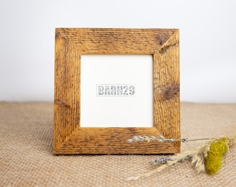 Könnte beinhalten: Ein rustikaler Holzbilderrahmen mit einer natürlichen Holzoptik. Der Rahmen ist quadratisch und hat ein schlichtes Design. Der Rahmen steht auf einer Jutestoff-Oberfläche mit getrockneten Blumen im Vordergrund. Der Rahmen hat einen weißen Passepartout und der Text "BARN29" ist in der Mitte des Passepartouts gedruckt.