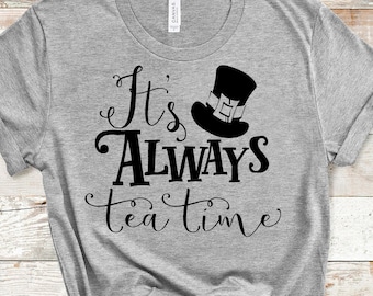 Può includere: Una maglietta grigia con testo nero che recita "It's Always tea time" e una silhouette nera di un cappello a cilindro con una fascia verde.