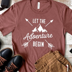 May include: A maroon t-shirt with white text that reads "Let the Adventure Begin" with a mountain and arrow graphic.