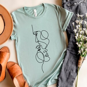 May include: A light blue t-shirt featuring a black line drawing of two faces intertwined.