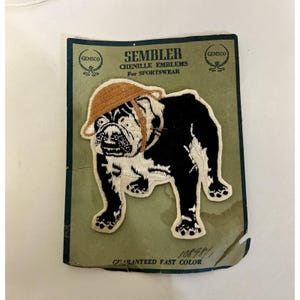 May include: Chenille emblem for sportswear featuring a black and white bulldog wearing a tan hat. The emblem is on a green and blue card with the text "SEMBLER" and "GUARANTEED FAST COLOR". The emblem is from GEMSCO.