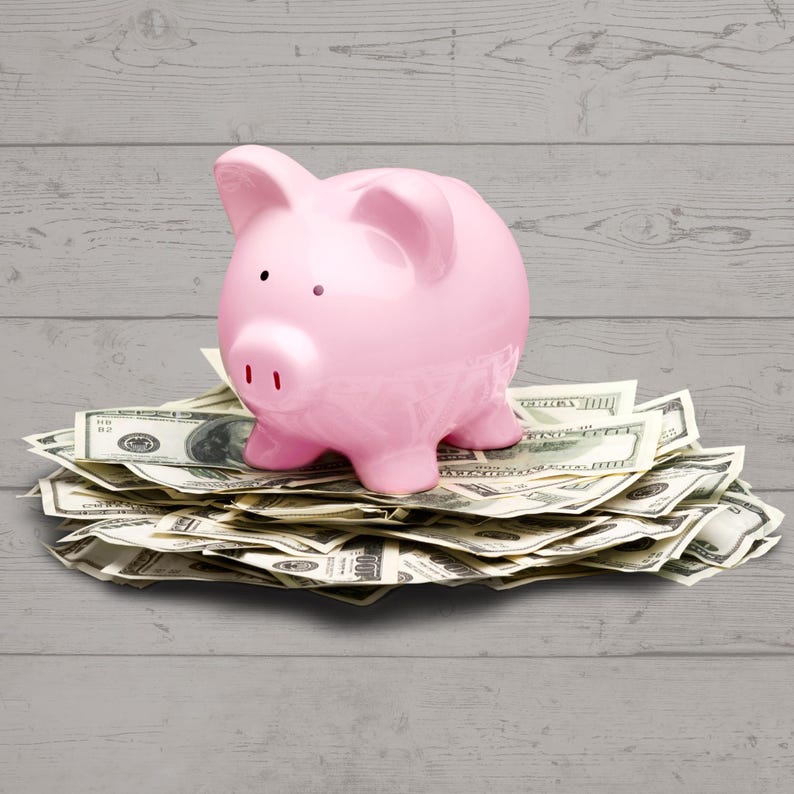 May include: A pink piggy bank sitting on a pile of US dollar bills.