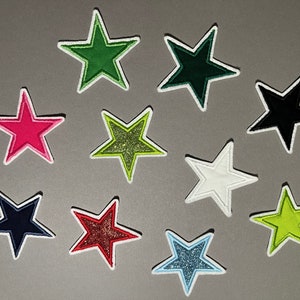Könnte beinhalten: Zehn verschiedene sternförmige Bügelbilder in verschiedenen Farben, darunter Grün, Schwarz, Pink, Weiß, Blau und Rot. Einige der Sterne haben Glitzer.