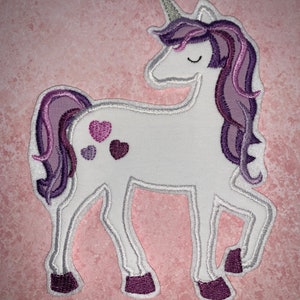 Könnte beinhalten: Weißer Einhorn-Applikator mit lila Mähne und Schwanz. Das Einhorn hat ein silbernes Horn und drei lila Herzen an der Seite.
