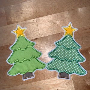 Könnte beinhalten: Zwei grüne Weihnachtsbaum-Anhänger mit gelben Sternen oben. Ein Baum hat ein einfarbig grünes Design und der andere ein weißes Punkte-Design.