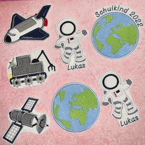 Könnte beinhalten: Ein Set Bügelbilder mit einem Raumschiff, einem Rover, einem Satelliten, zwei Astronauten und zwei Globen mit dem Text "Schulkind 2022" und "Lukas".