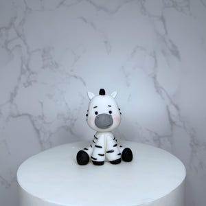 A small white figurine of a zebra sitting on a white surface against a marble background.