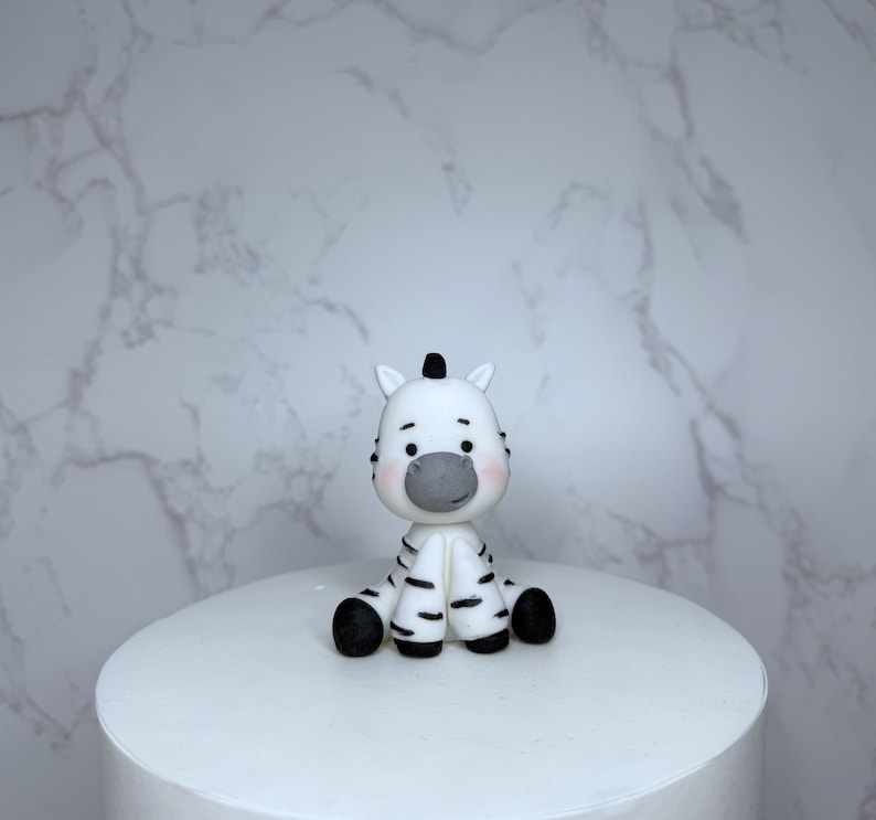 A small white figurine of a zebra sitting on a white surface against a marble background.