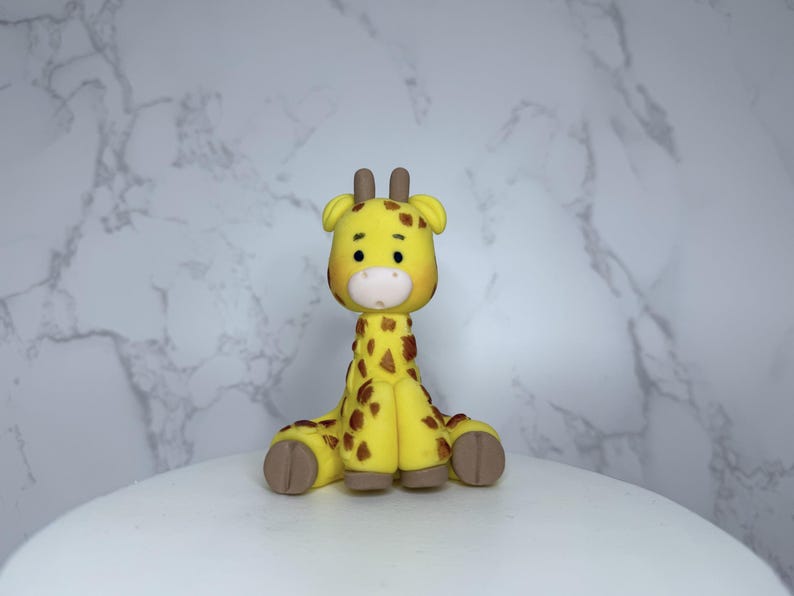 A yellow and brown giraffe figurine is sitting on a white surface against a marble background.