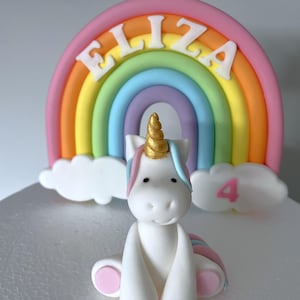 A white cake with a white unicorn figurine and a rainbow-colored cake topper.