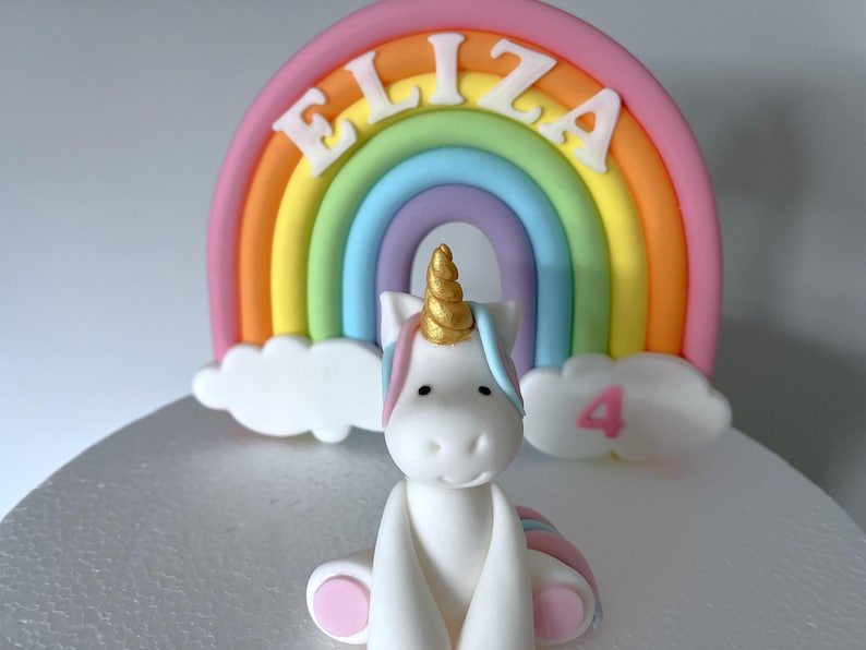 A white cake with a white unicorn figurine and a rainbow-colored cake topper.