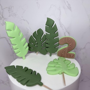 A cake with green leaf-shaped decorations and a brown number 2 candle on top, set against a marble background.