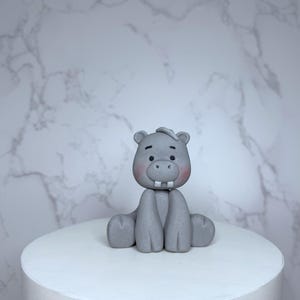 A gray ceramic hippo figurine is sitting on a white pedestal against a marble background.