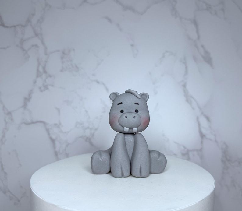 A gray ceramic hippo figurine is sitting on a white pedestal against a marble background.
