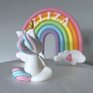 A white cake with a white unicorn figurine and a rainbow-colored arch in the background.
