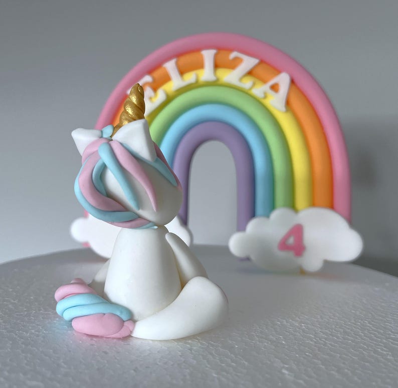 A white cake with a white unicorn figurine and a rainbow-colored arch in the background.
