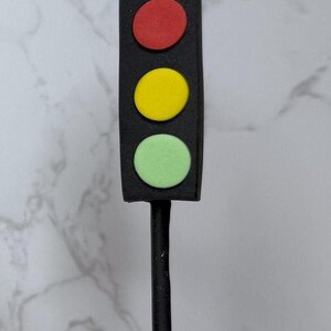 A black traffic light with three colored lights (red, yellow, and green) is mounted on a black pole, which is placed on a white surface.