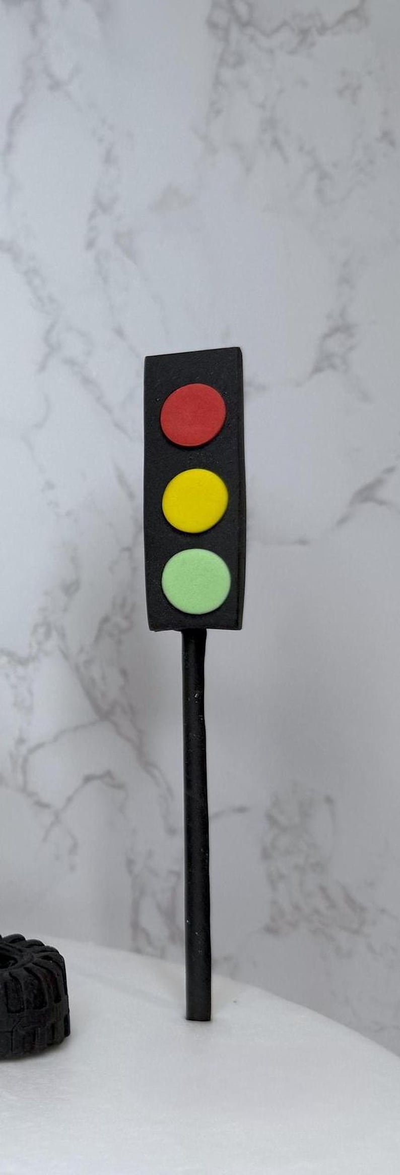 A black traffic light with three colored lights (red, yellow, and green) is mounted on a black pole, which is placed on a white surface.
