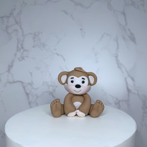 A small brown monkey figurine sitting on a white cake.