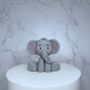 A gray elephant figurine is sitting on top of a white cake.