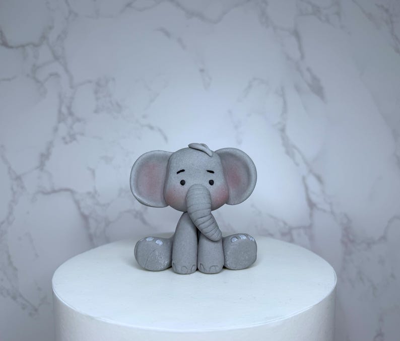 A gray elephant figurine is sitting on top of a white cake.