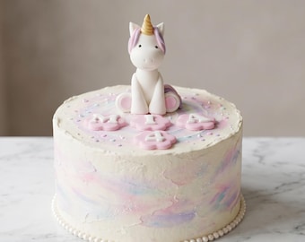 May include: A round cake with white icing, decorated with pastel pink, blue, and purple swirls. A white unicorn figurine with a gold horn and pink mane sits on top. Pink flower decorations with the number "4" are also on the cake.