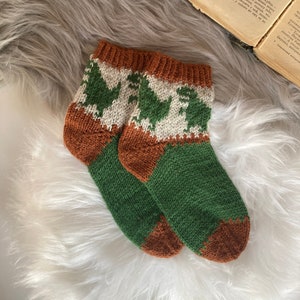 Könnte beinhalten: Ein Paar grüne und braune Stricksocken mit einem weißen und braunen Dinosauriermuster.