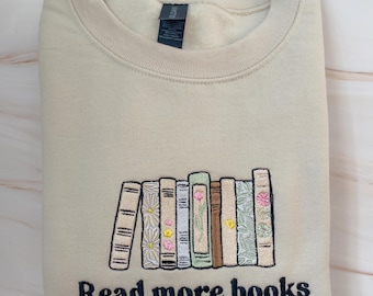 May include: A beige sweatshirt with embroidered text that reads "Read more books". The embroidery features a row of colorful books with floral details.