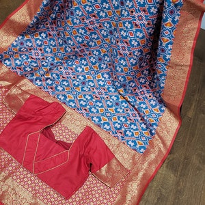Ikkat Patola saree in a stunning blue and red combination with weaving work over the body and a grand pallu. Stitched blouse included.