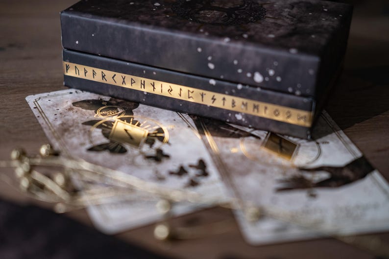 Puede incluir: Una caja negra con letras doradas y fondo blanco. La caja est&aacute; cerrada y se encuentra encima de una pila de cartas blancas con detalles dorados. Las cartas tienen un aspecto desgastado y vintage.