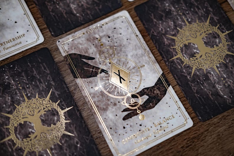 Puede incluir: Una carta del tarot con fondo blanco y detalles dorados. La carta representa dos manos que se acercan la una a la otra, con un s&iacute;mbolo de cruz en forma de diamante en el centro. La carta se titula "G&eacute;minis" y el texto "Encontrar el equilibrio" est&aacute; impreso en la parte inferior.