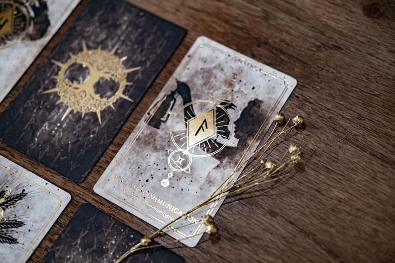 Puede incluir: Una carta de tarot con un dise&ntilde;o dorado y negro. La carta se llama "Wisdom Communication" y presenta una imagen estilizada de dos figuras con un s&iacute;mbolo en el centro. La carta est&aacute; sobre una superficie de madera con una ramita de flores secas.