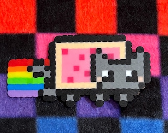 May include: A pixel art style cat figure made of fused plastic beads. The cat has a grey head and body, a rectangular pink body with dark pink spots, and a trail of horizontal rainbow stripes in red, orange, yellow, green, blue, and purple.