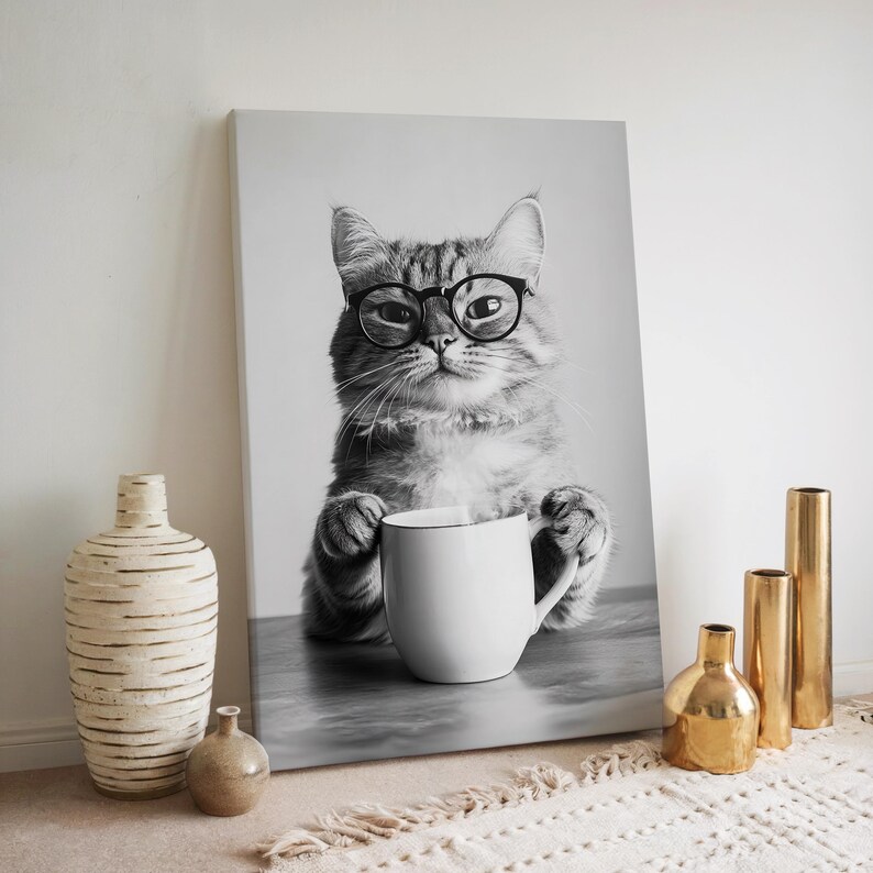 Op de afbeelding: Zwart-witfoto van een kat met een bril die een witte mok vasthoudt. De kat zit op een grijs oppervlak.