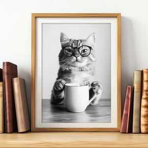 Op de afbeelding: Zwart-witfoto van een kat met een bril die een witte mok vasthoudt. De kat zit aan een tafel met een boekenkast op de achtergrond.