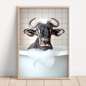 Puede incluir: Impresión enmarcada de un ñu negro en una bañera blanca, cubierto de burbujas blancas. El animal tiene cuernos grandes y curvados y mira directamente al espectador. El fondo es una pared alicatada.