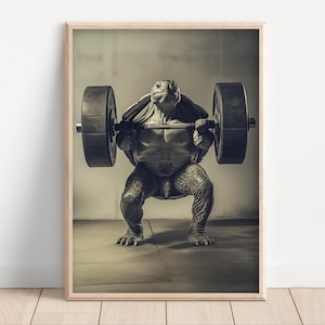 Op de afbeelding: Een zwart-wit afdruk in een houten lijst van een gespierde schildpad die een halter optilt. De schildpad staat in een squat positie. De afbeelding is geschikt voor een sportkamer of als decoratie.